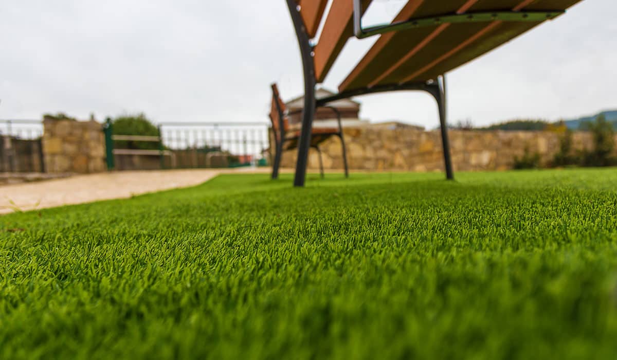 Lush artificial grass with benches nearby.